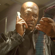 Samuel L. Jackson wears a leather jacket and black t-shirt while holding a corded phone in one hand and a large snake in the other in Snakes on a Plane.
